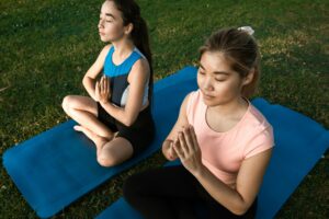 Two women meditating on a yoga mat in the park